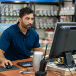 Latin American business manager using a laptop computer while working at a hardware store - small business concepts